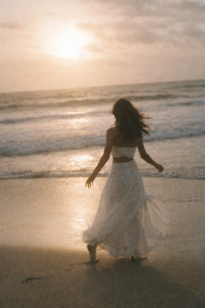 Calm beach at golden hour, figure in white walking on the sand, open sky